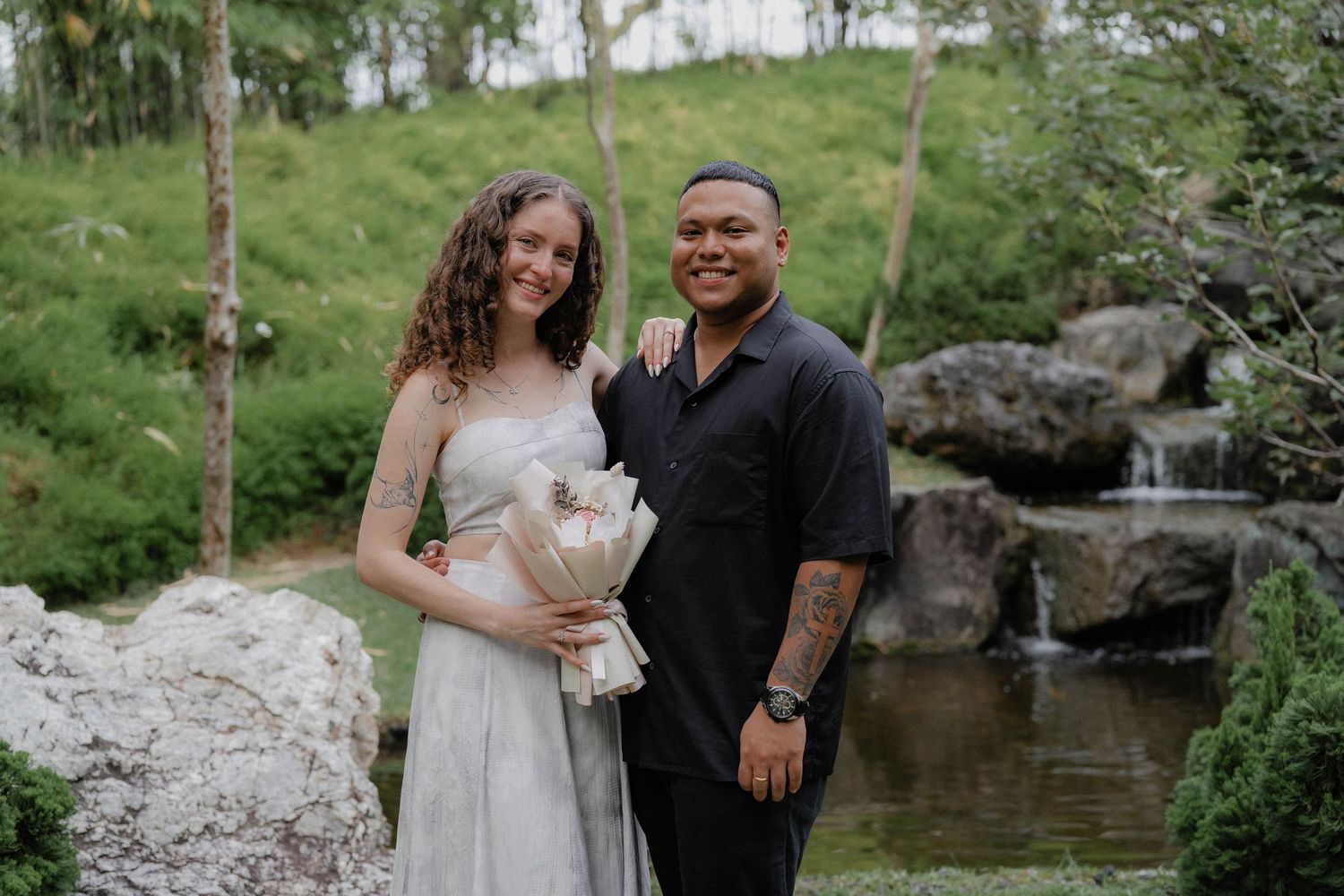 A happy couple posing together by a waterfall in a tropical garden setting.