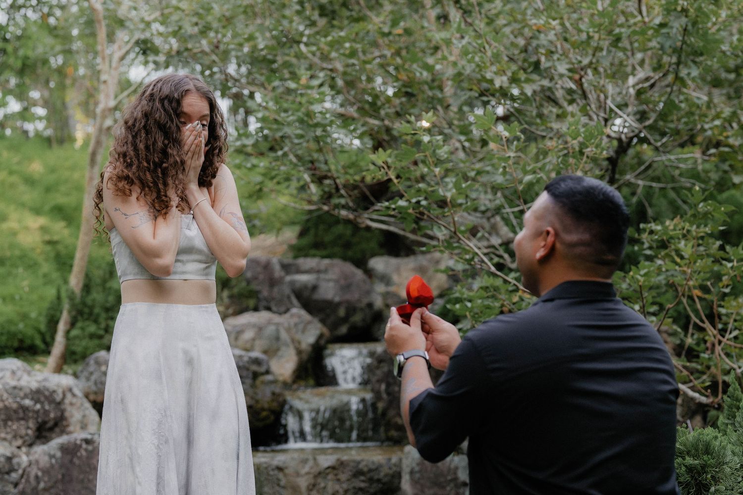A couple interacts playfully near a rock garden with flowing water.