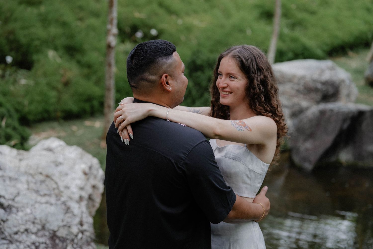 Happy couple embracing by a rocky stream in a lush green park.