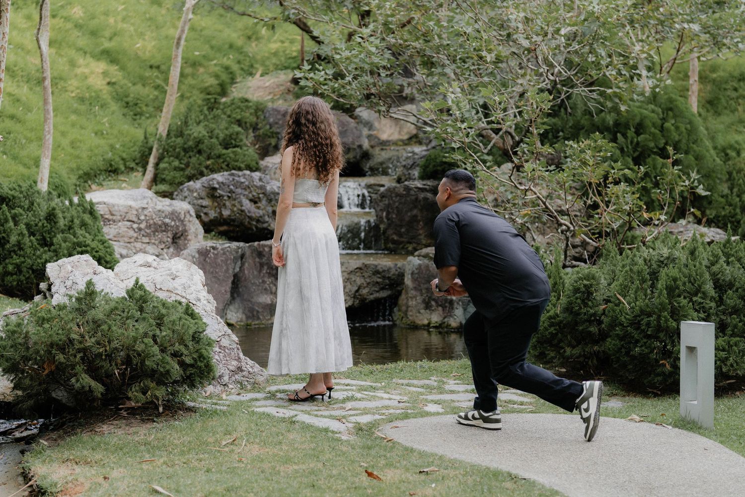 A playful wedding photoshoot scene in a garden setting with rocks and greenery.