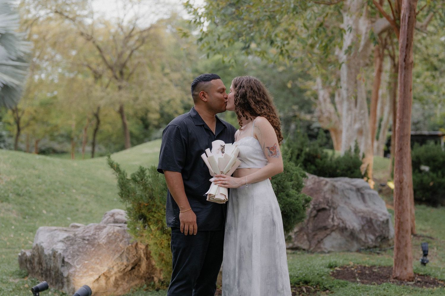 Couple celebrating their engagement in a scenic park with trees and rocks.
