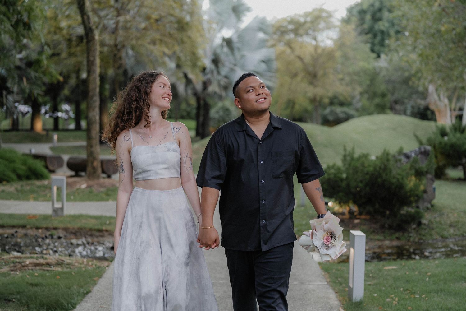 A couple walking hand in hand along a garden path surrounded by greenery.
