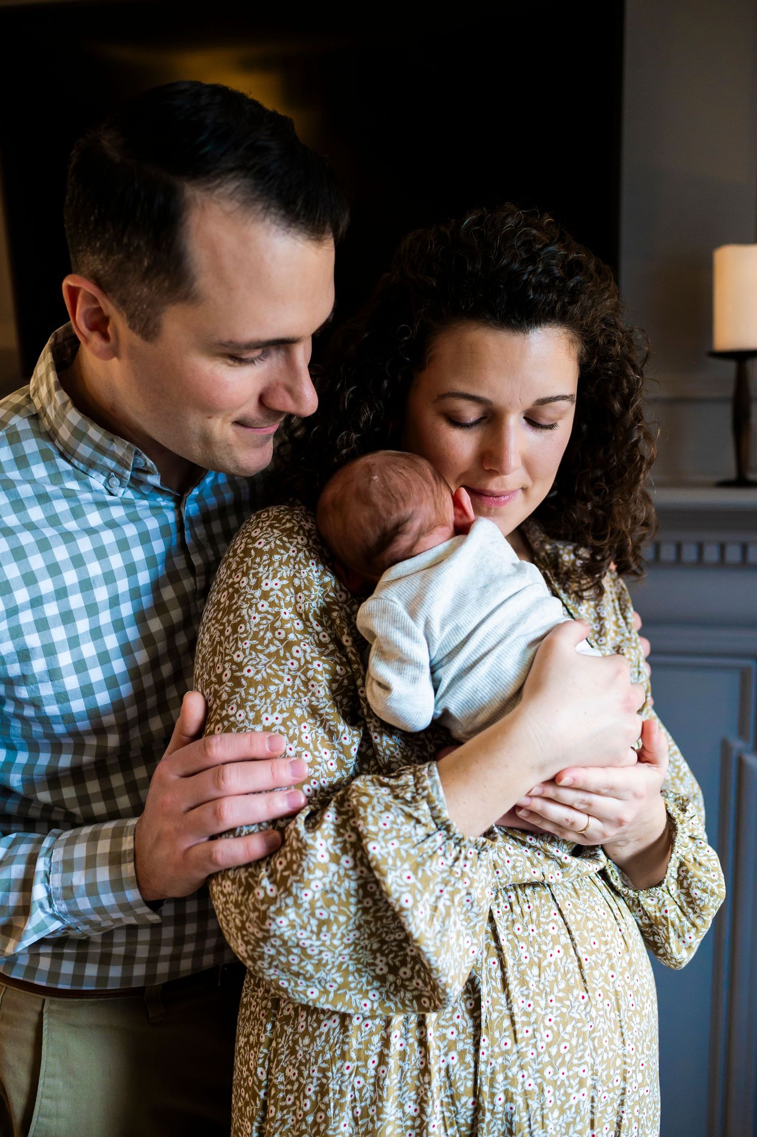 New parents share an intimate moment while cuddling their sleeping newborn baby at home.