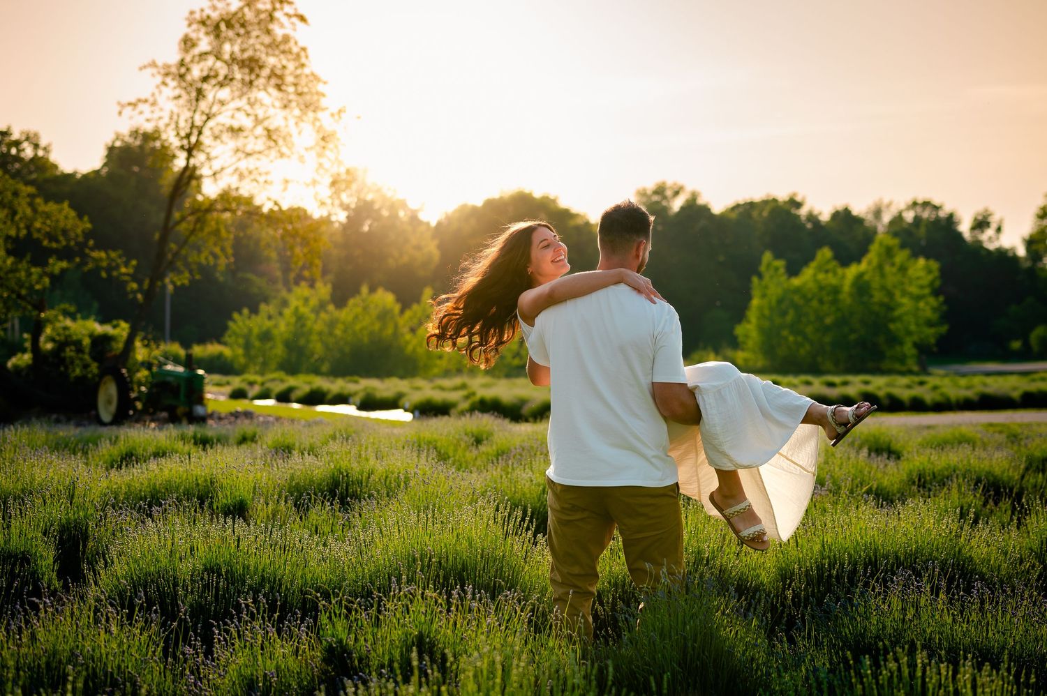 Two people dancing together in a lavender field at sunset with golden sunlight streaming through the trees.