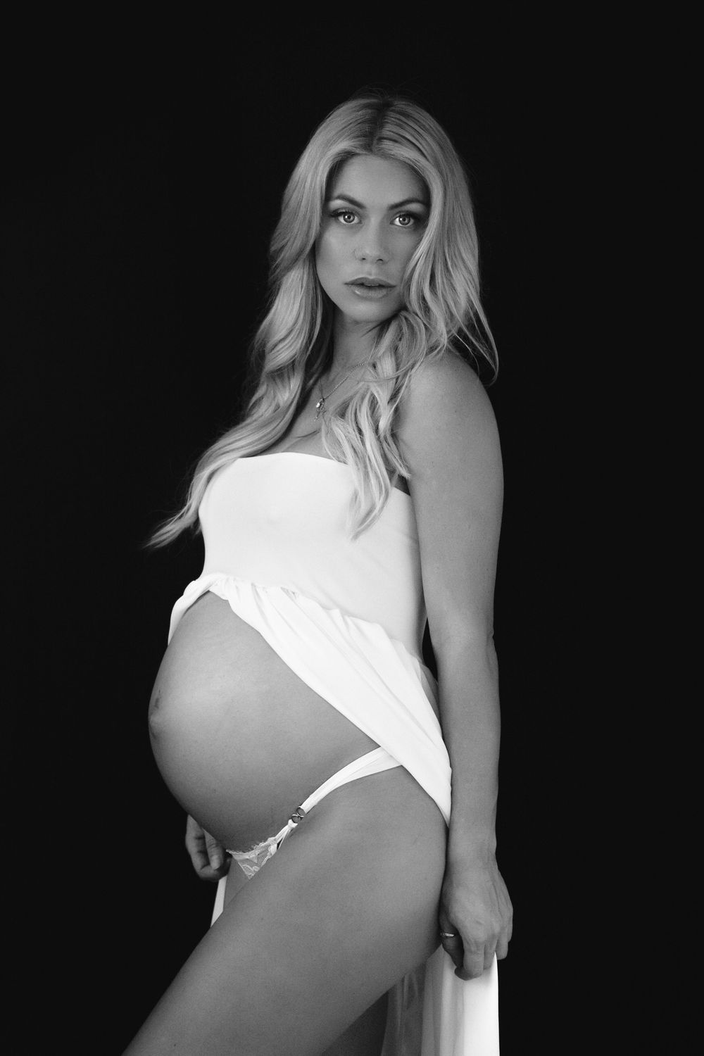 Gold Coast studio maternity session with a black backdrop pregnant lade wearing our white strapless gown with open front photo is black andt