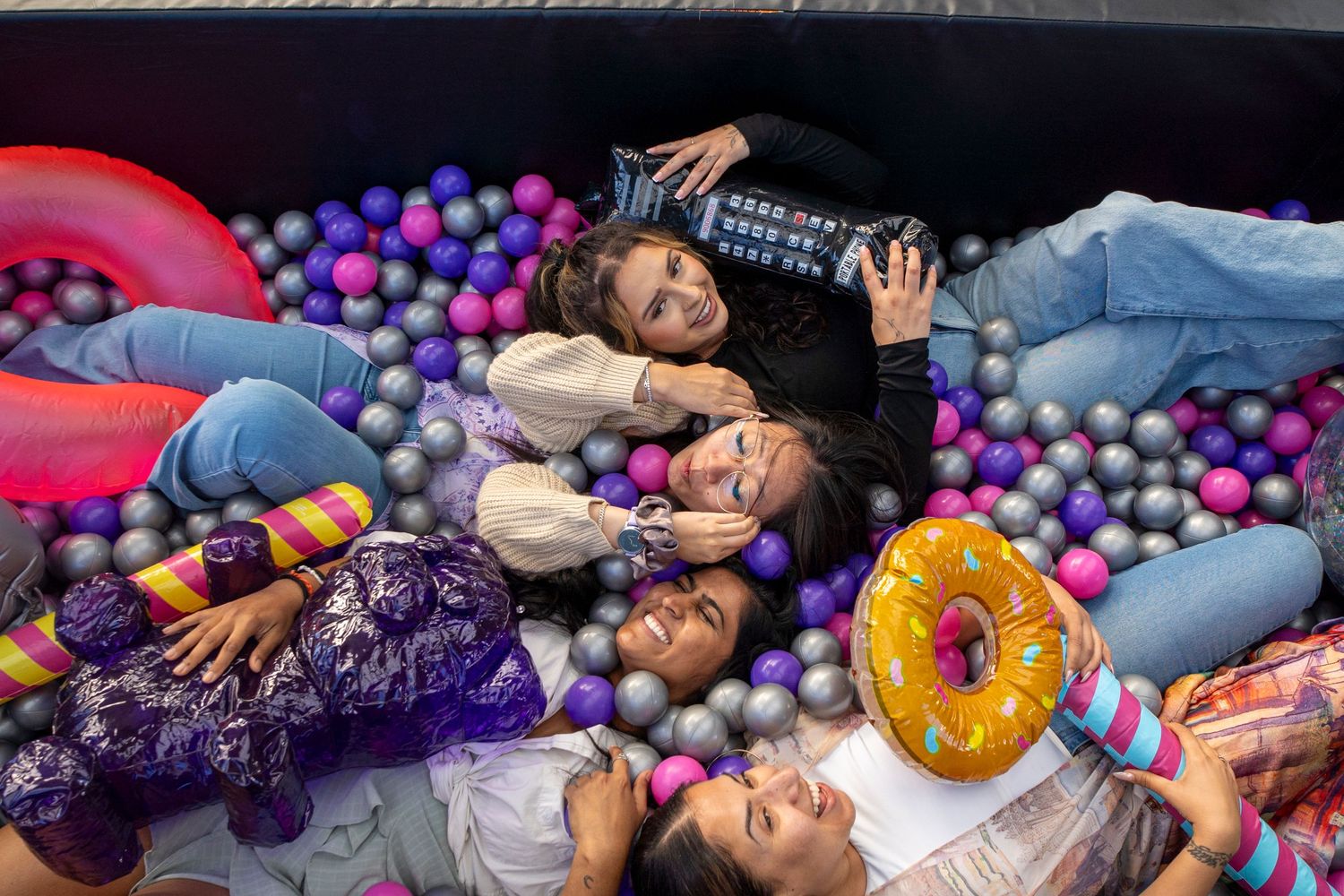 People having fun in a colorful ball pit with inflatable toys and floating donuts.