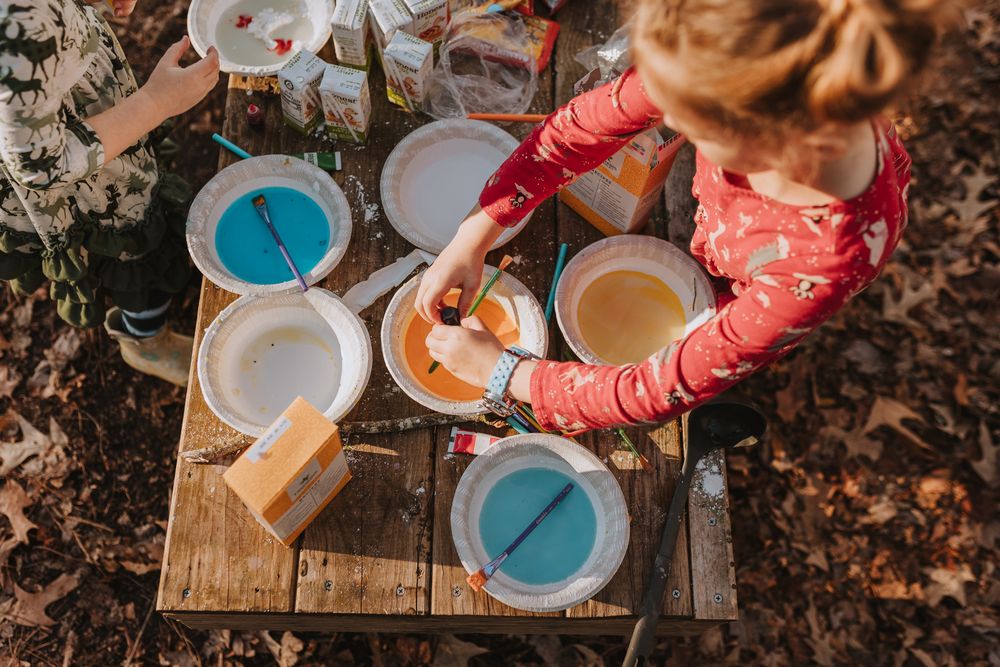 Overhead view of someone in a pink sweater painting with turquoise and white paint on a rustic wooden surface outdoors. Whitney Popp