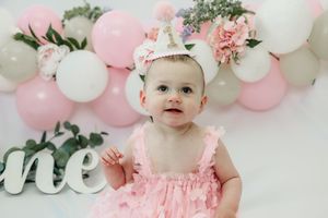 Pink and white balloon garland decorates a festive cake smash photography session with floral accents and greenery.