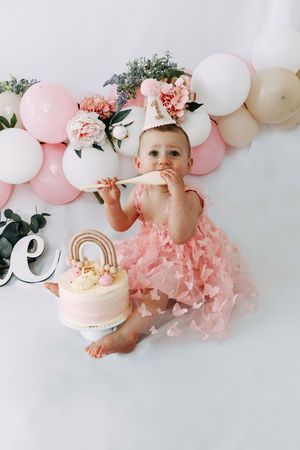 First birthday celebration setup with pink tulle dress, balloon arch, and white cake with gold rainbow decoration.