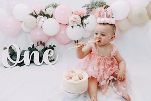 Pink and white balloon decorations and party decor set up for a first birthday celebration with cake.