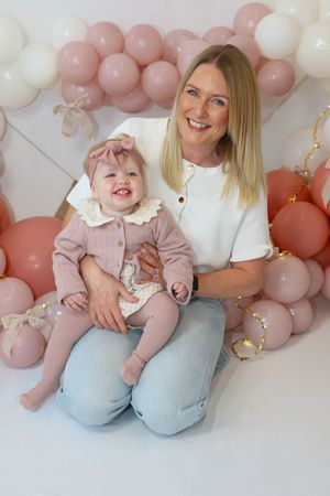 A baby and adult sit together against a pink and white balloon backdrop in a series of candid moments.