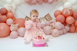 Pink and white balloon garland with cake decorations creates an elegant first birthday party backdrop.