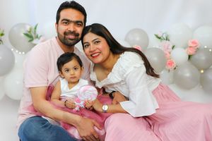 A family celebrates a special occasion in a pink and white decorated setting with balloons and flowers.