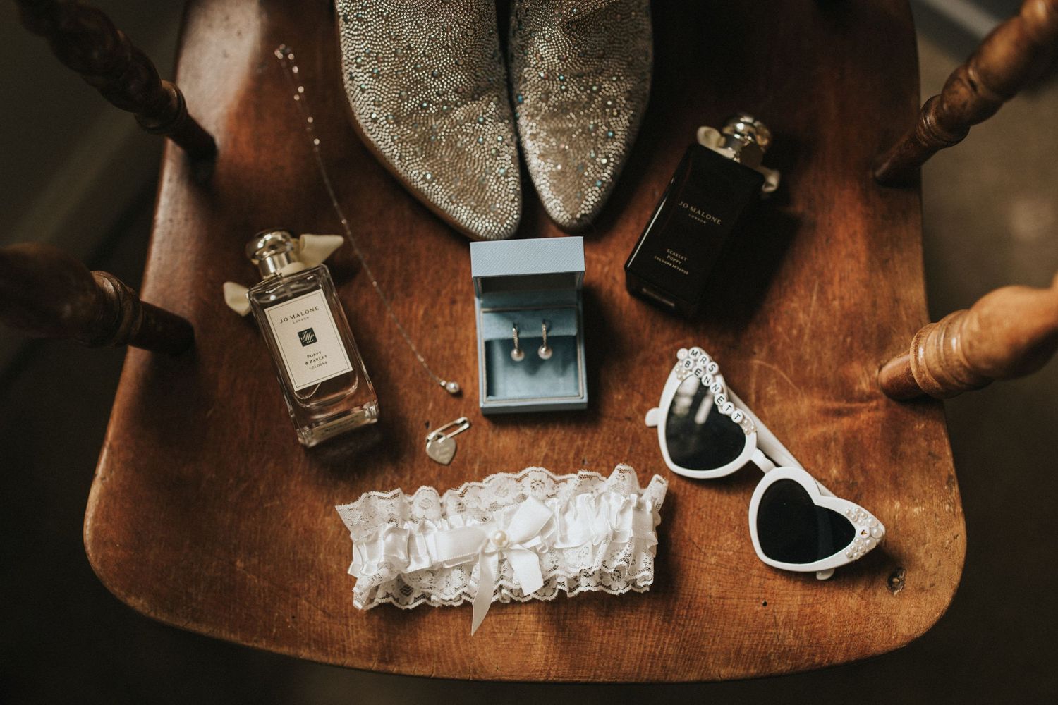 Wedding accessories including perfume bottles, sunglasses, rings and jewellery arranged on a rustic wooden surface.