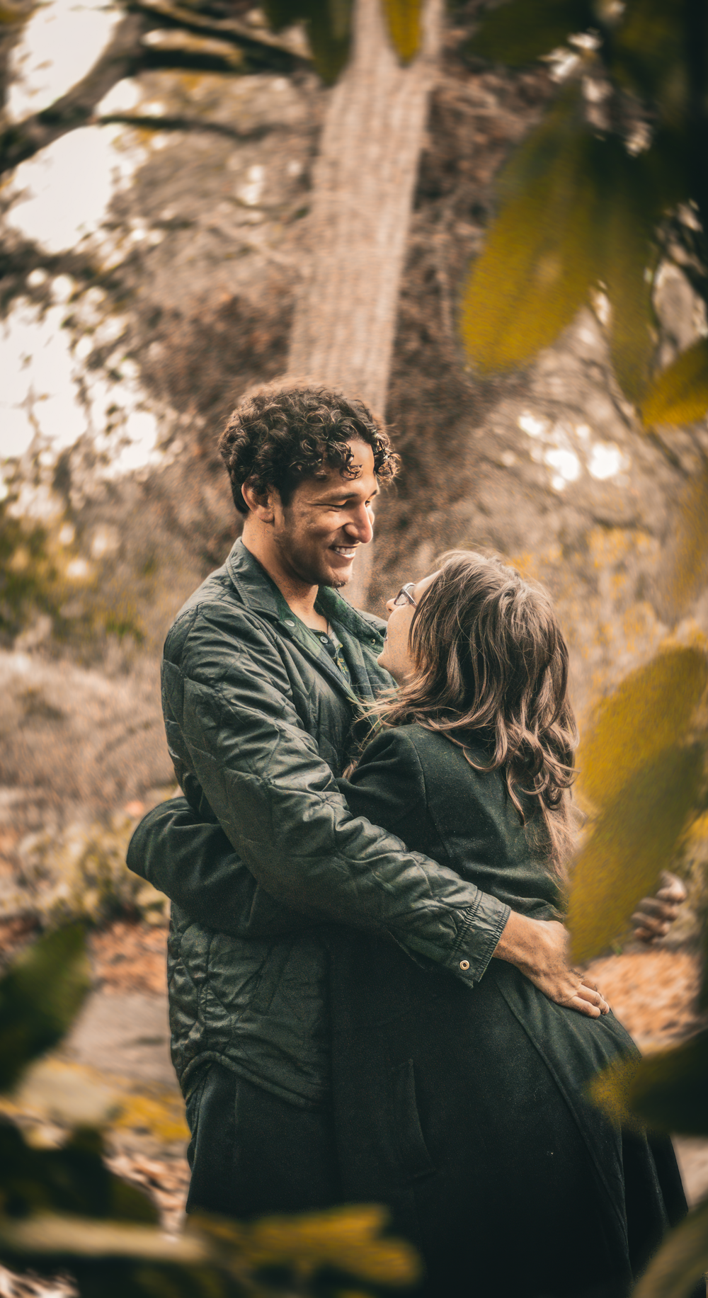 A couple embraces lovingly in a romantic autumn setting with golden leaves framing the candid outdoor scene.