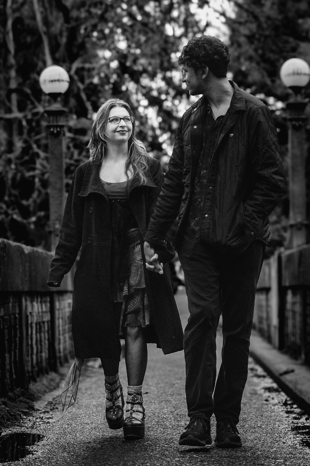 A couple walking together and laughing along a tree-lined path in a black and white artistic photograph.