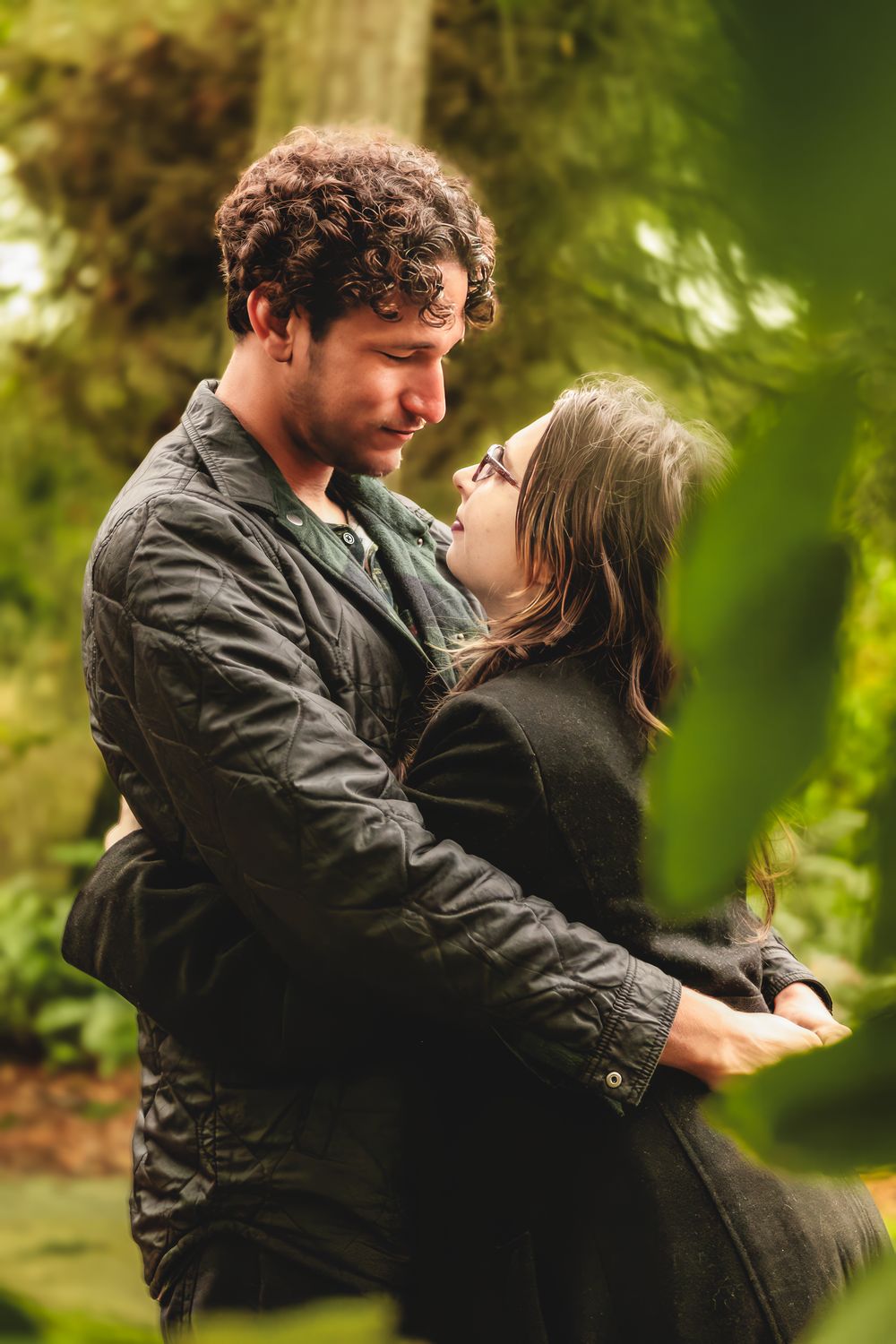 Romantic couple embraces in garden setting with soft green bokeh background and natural lighting.