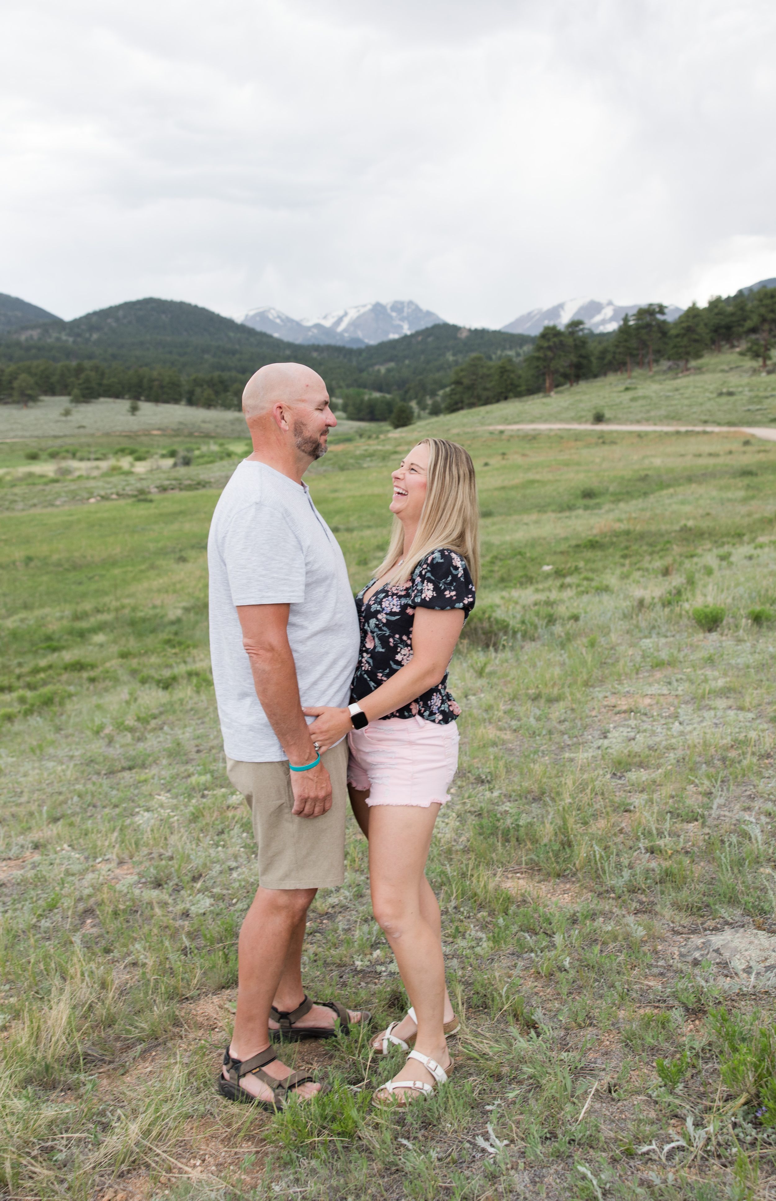 A couple shares a romantic moment in a mountain meadow with snow-capped peaks in the distance.