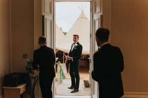People standing in a doorway at a wedding venue with tipis in the background at Hirst Priory.