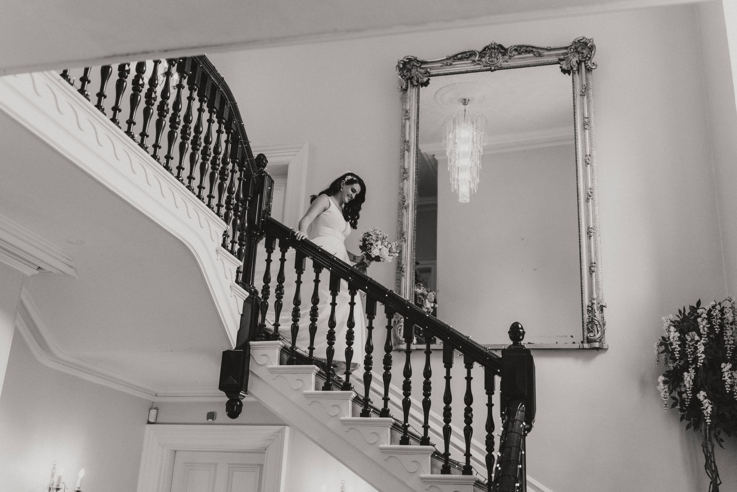 Black and white vintage photograph showing a bride descending down a grand staircase at Hirst Priory.