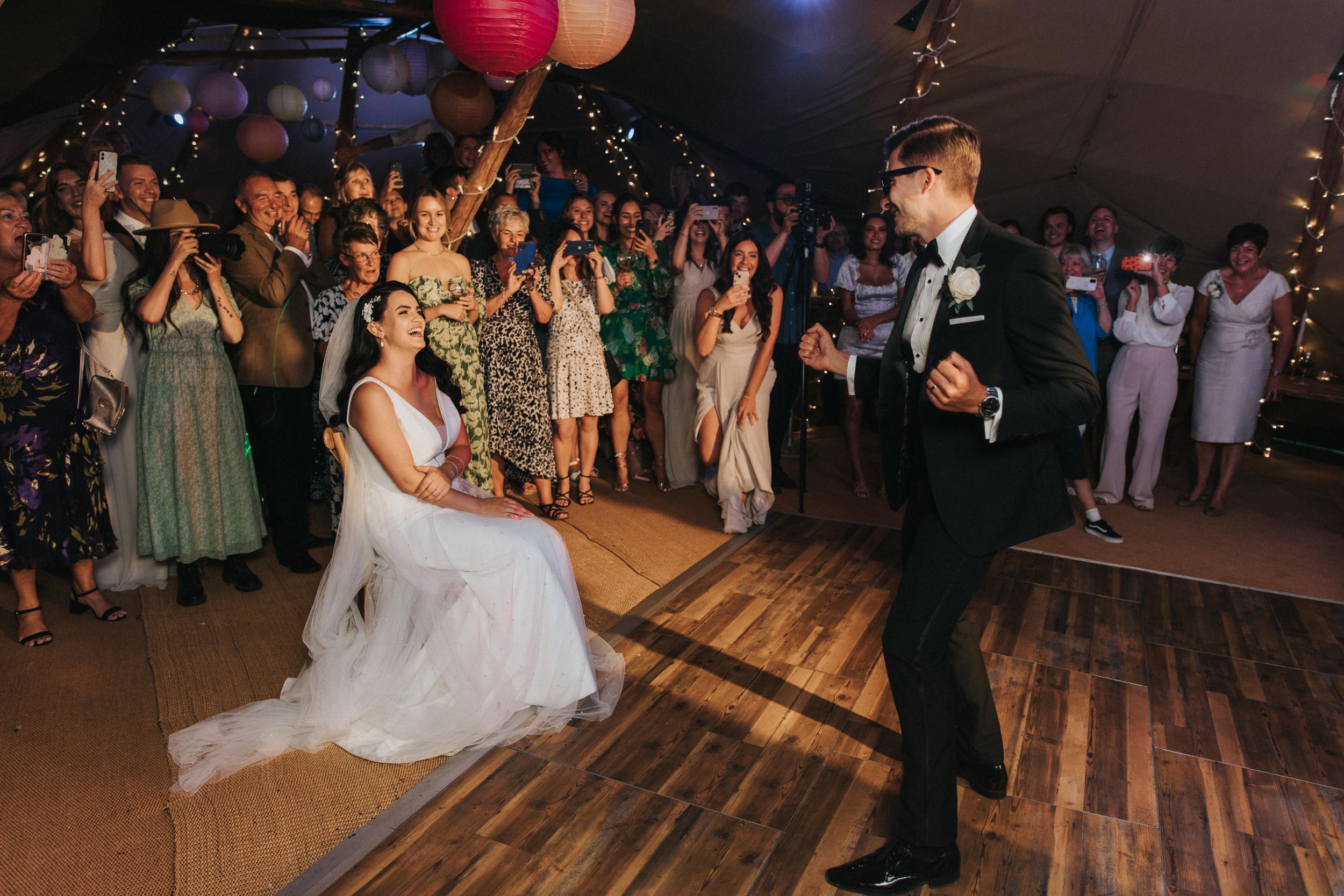 Party guests dance  on a wooden dance floor at an elegant indoor reception venue with festive lighting and decor at Hirst Priory.
