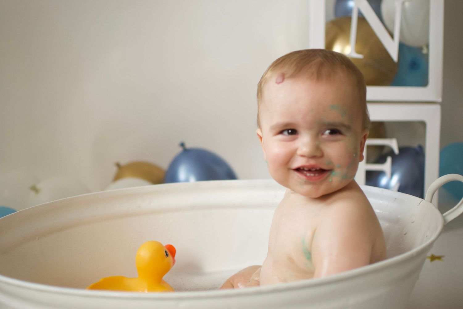Baby splashes in vintage bathtub during milestone photo session with blue decor.