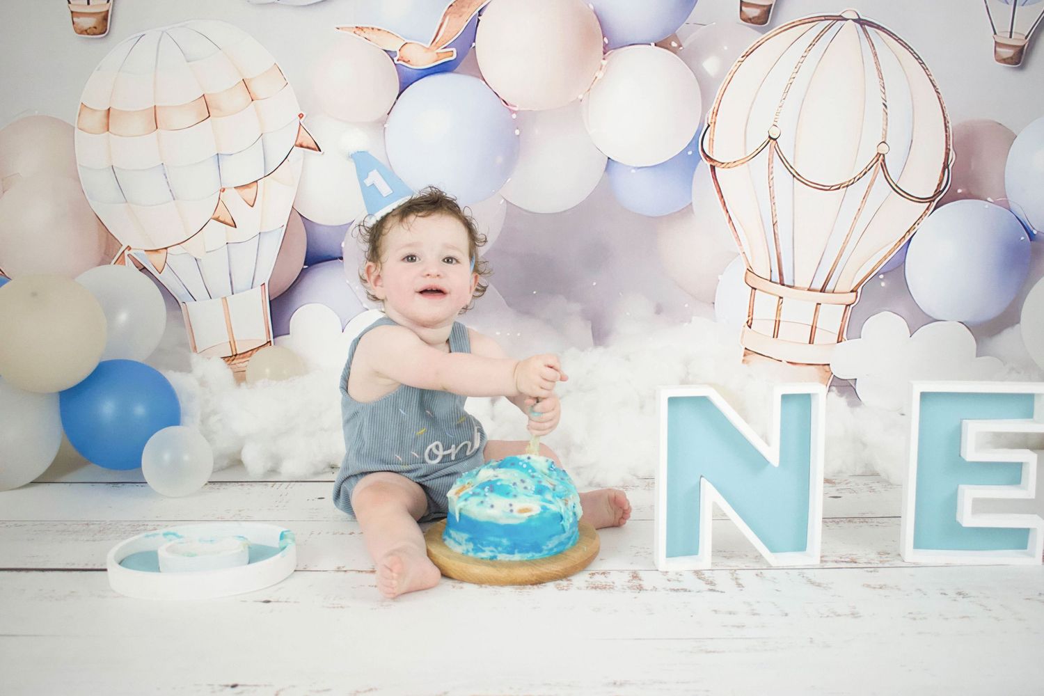 Baby splashes in vintage bathtub during milestone photo session with blue decor.