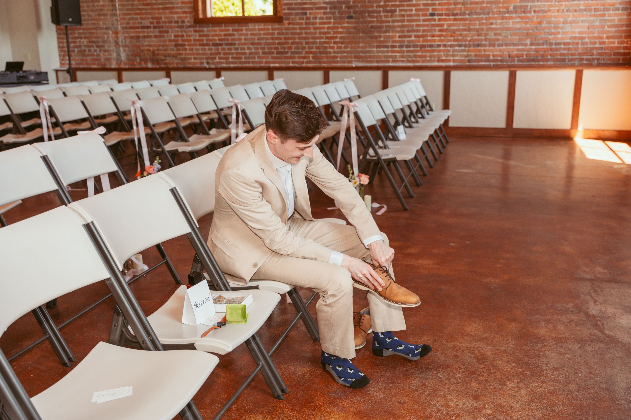 A row of empty beige folding chairs arranged in a room with rustic brick walls and wooden flooring.