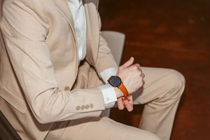 Person in beige suit adjusts their tie while sitting in vintage setting.