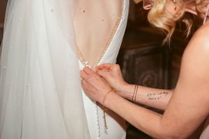 Close-up detail of hands adjusting a white wedding dress with delicate fabric and elegant detailing.