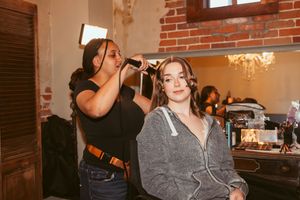 Professional makeup artist working on hair styling in a vintage brick studio setting.