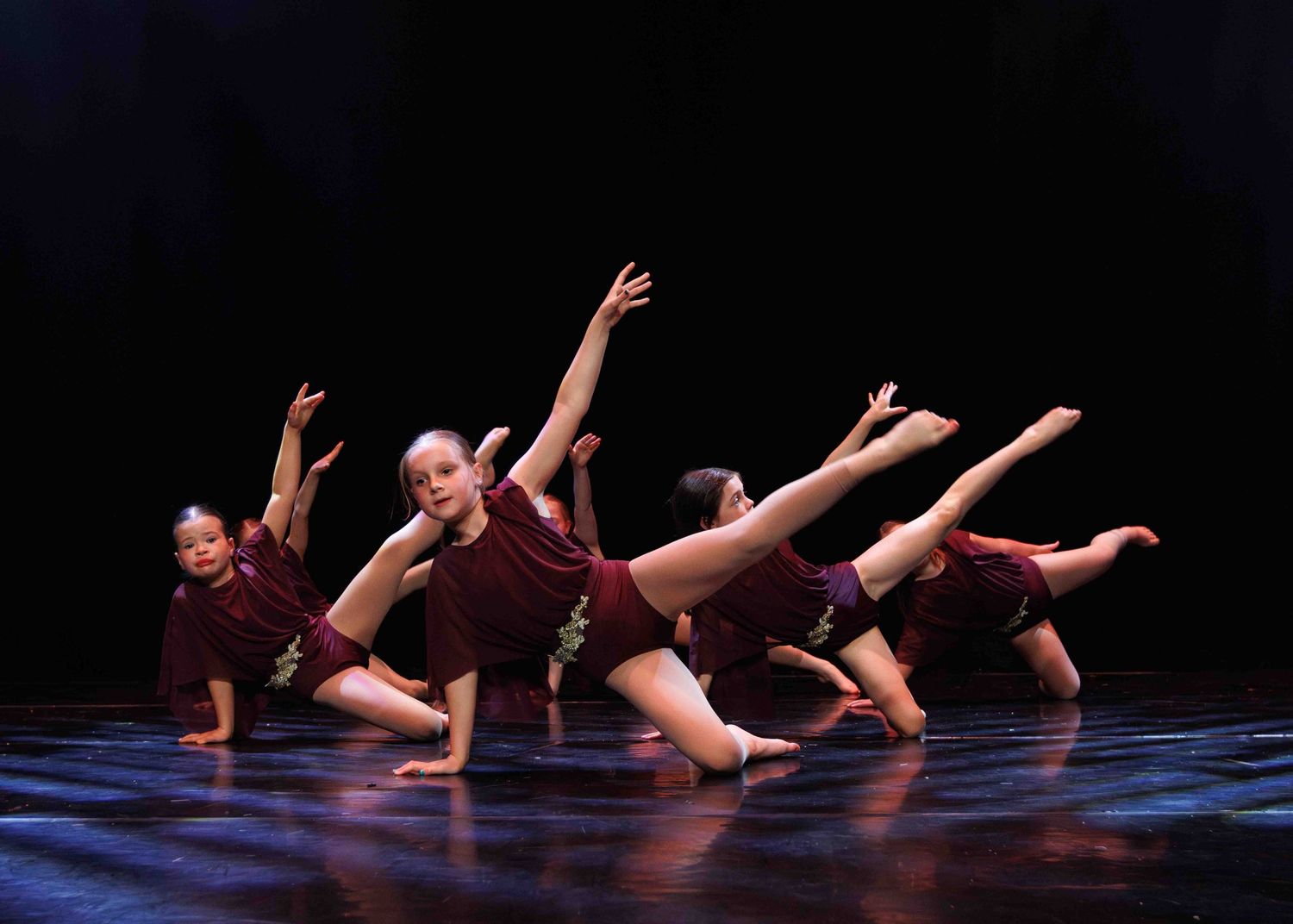 Contemporary dancers perform synchronized movements on the floor during dramatic dance sequence in a dark theater setting.