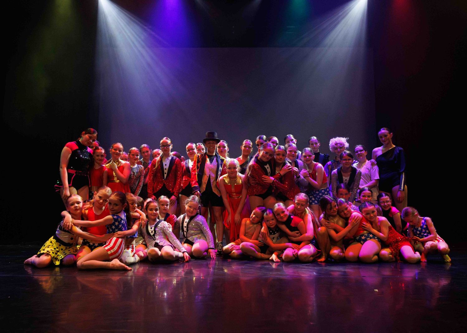 Group of performers lying on stage under dramatic purple and red lighting during dynamic dance recital performance.
