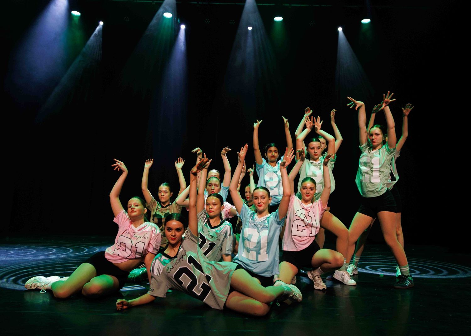 Dancers perform synchronized movements in a dimly lit theater stage with green lighting effects.