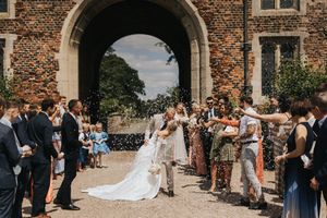 Panoramic view of a wedding ceremony at a historic stone church with guests gathered along the path.