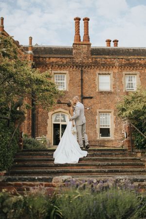 Historic brick mansion exterior with grand entrance steps surrounded by gardens creates a romantic wedding venue setting.