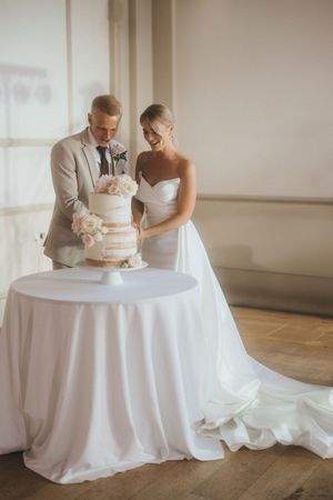 A wedding couple cuts into their elegant white tiered cake during their reception celebration.