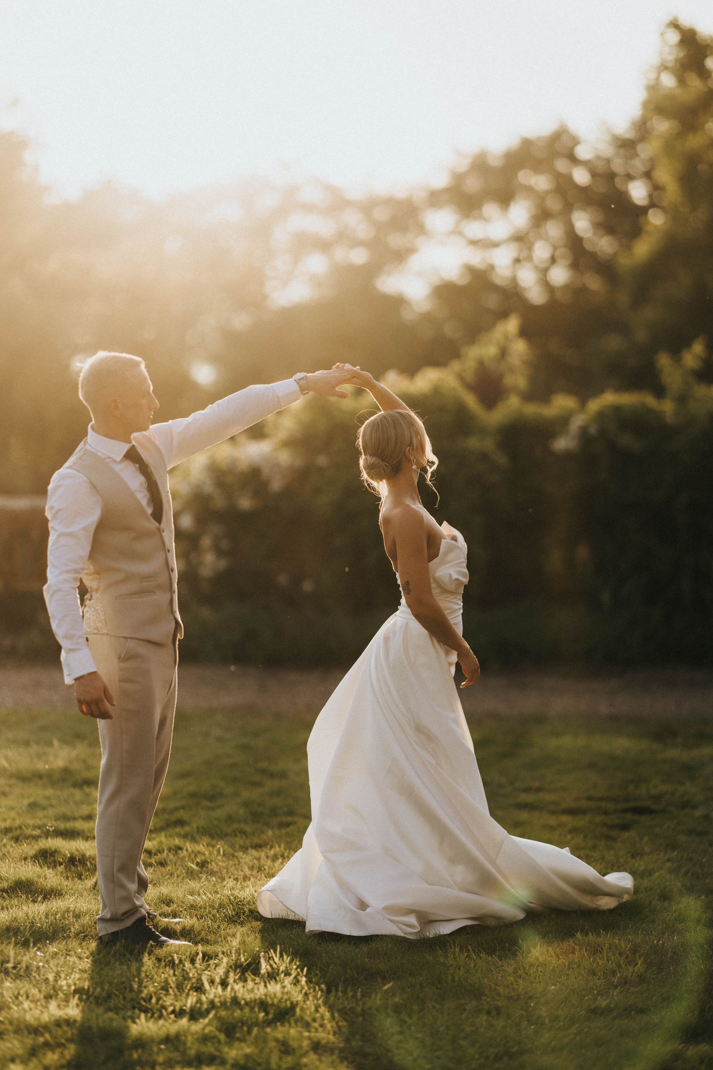 A bride and groom share a romantic moment at sunset in a grassy field with golden sunlight.