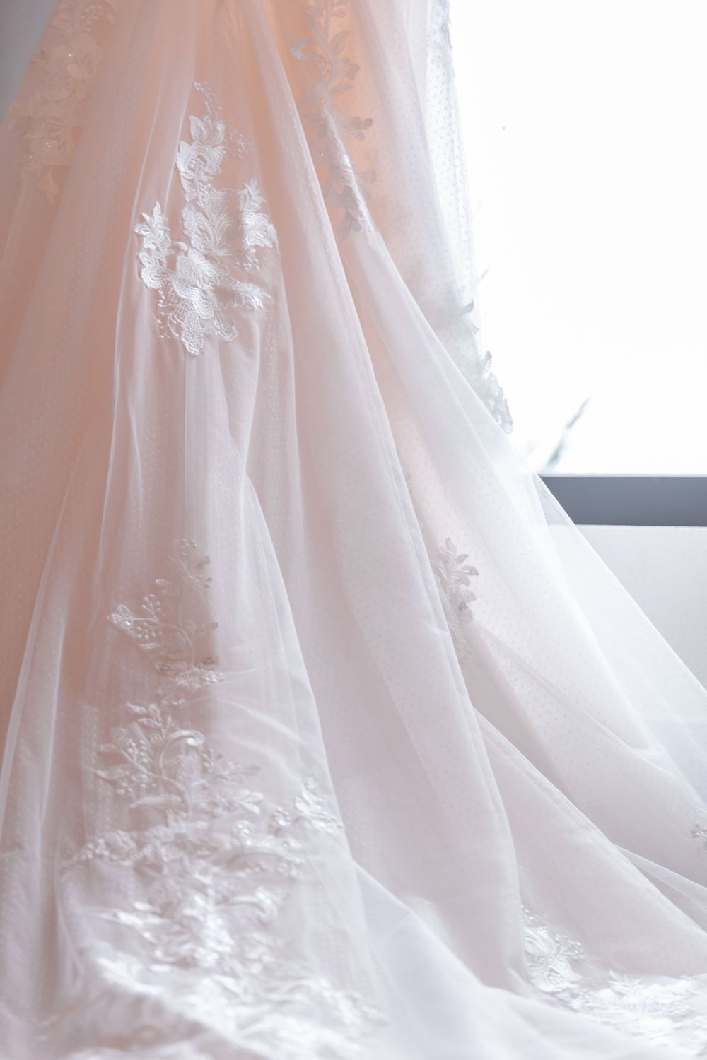 Delicate white floral lace details adorn the flowing tulle fabric of an elegant wedding gown.