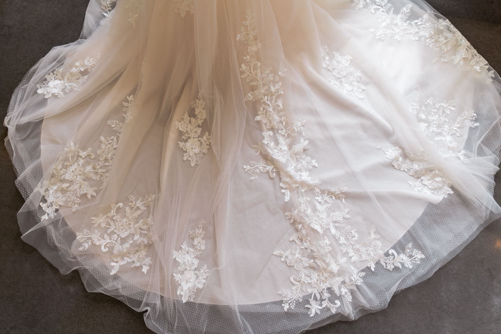 Delicate floral lace appliques adorn the flowing tulle skirt of an elegant white wedding gown.