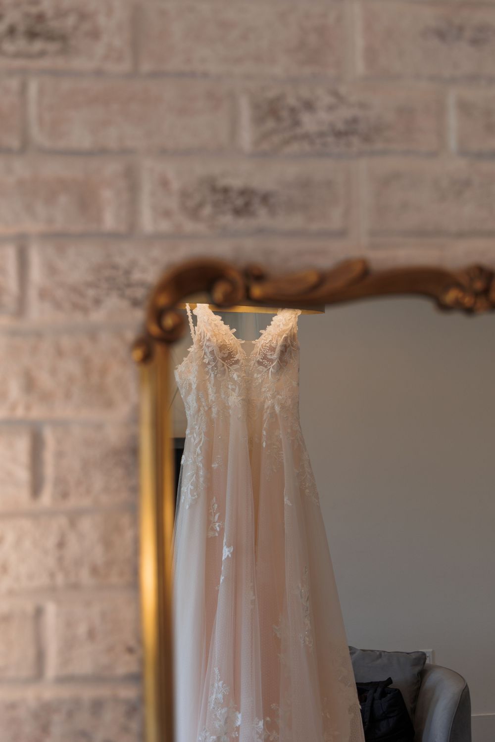 Wedding dress captured against a brick wall backdrop showing delicate lace details and a flowing white silhouette.