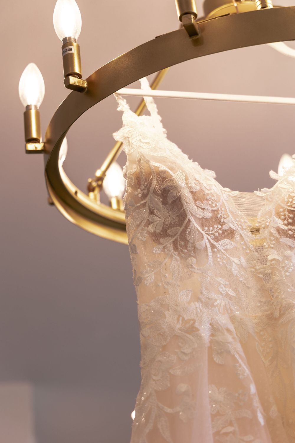 Close-up detail of delicate white lace trim on a wedding dress bodice with gold light fixture above.