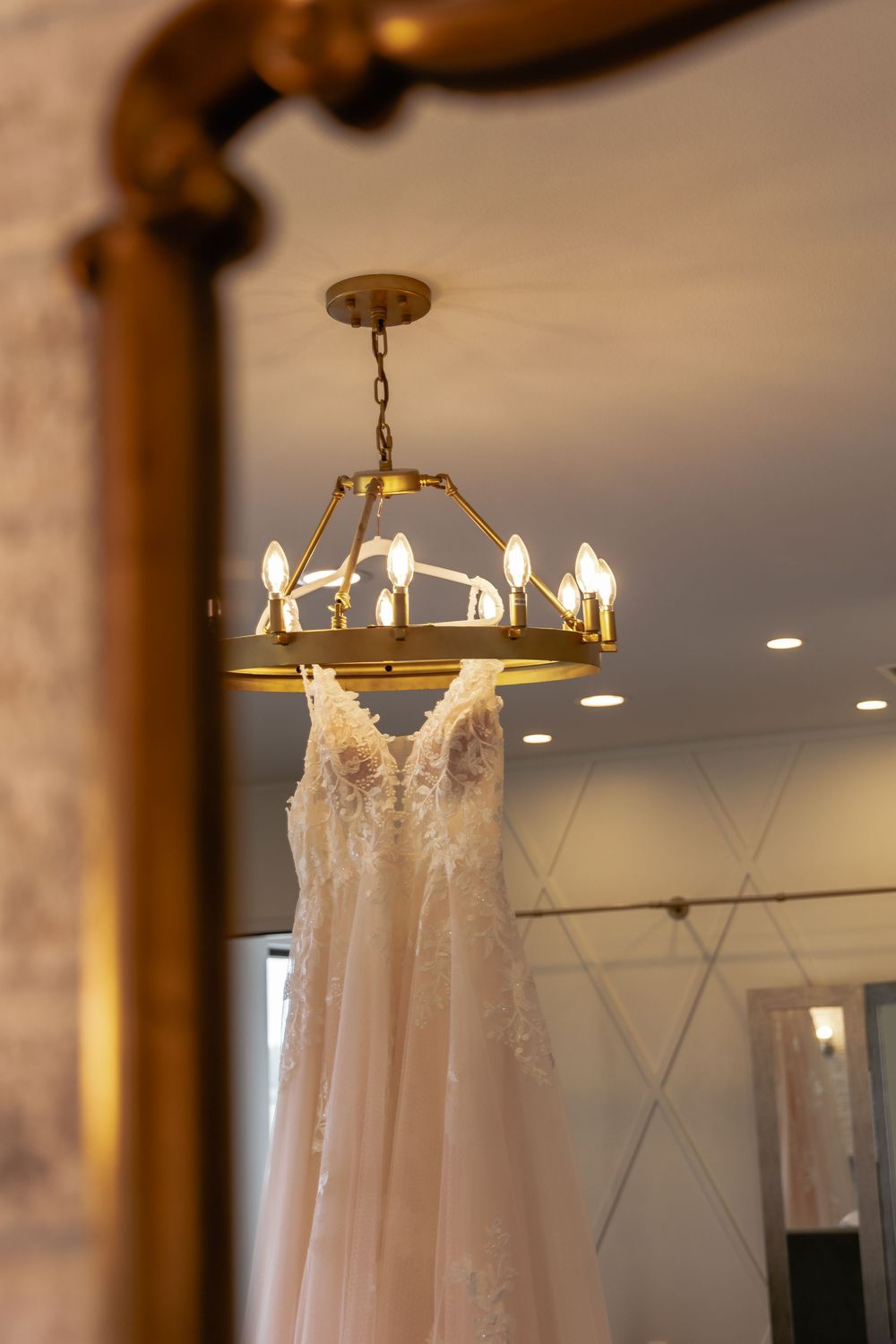White lace wedding dresses hanging from rustic wooden beams under elegant chandelier lighting.
