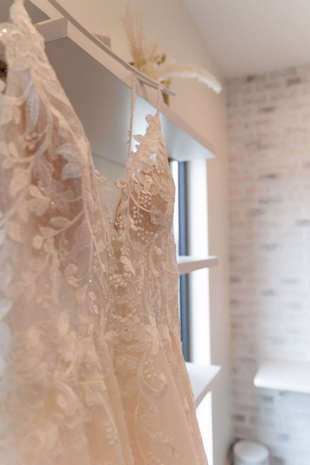 Delicate lace wedding dress with intricate floral details hanging in front of a window with natural light.