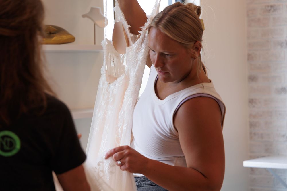 A person wearing a white tank top examines a mobile device in a room with white brick walls.