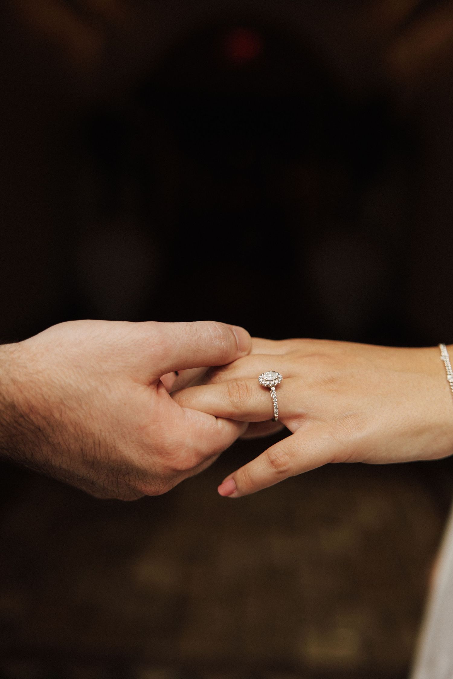A close-up shot of hands showing an engagement moment with a diamond ring being placed on a finger.