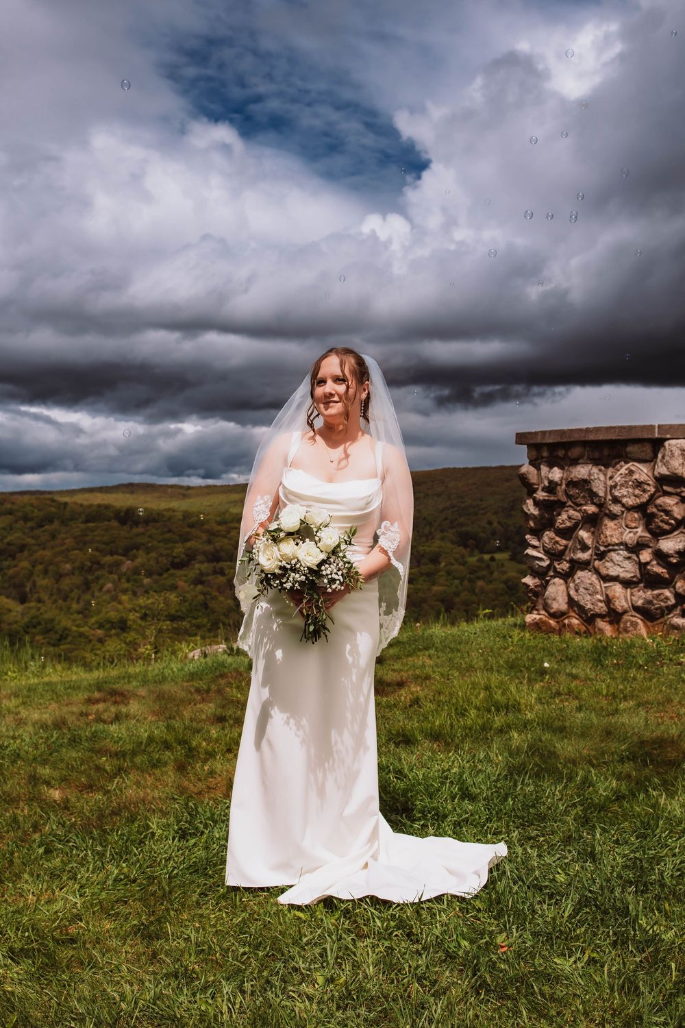Bride holding bouquet in front of minnewaska mountains at cragsmoor stone church
