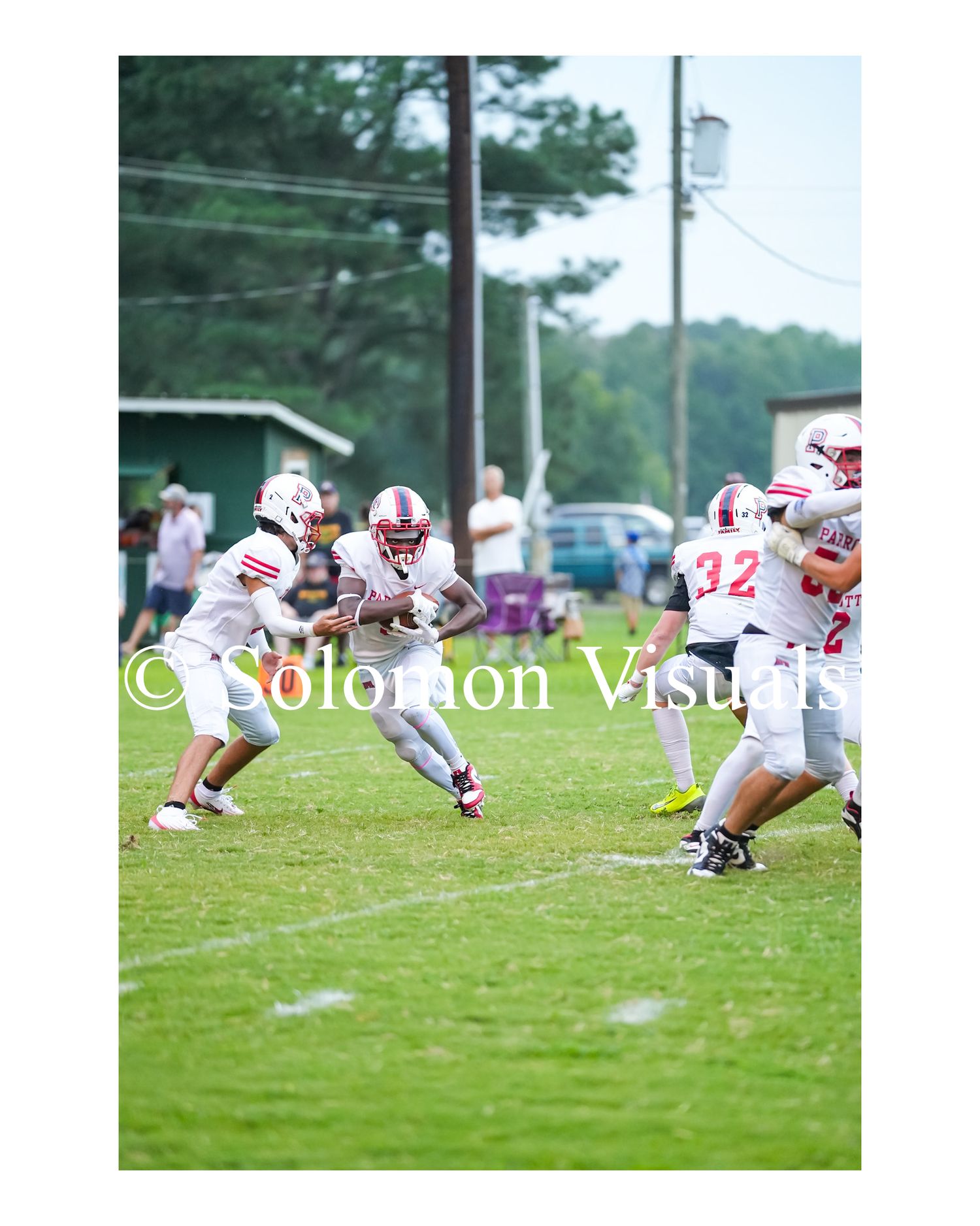 Football player in white uniform carries ball through blockers during outdoor game on grass.