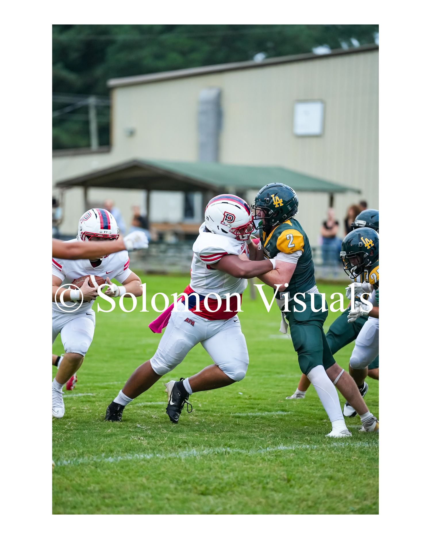 White-uniformed football player blocks green-jersey opponent during outdoor game near goalpost.