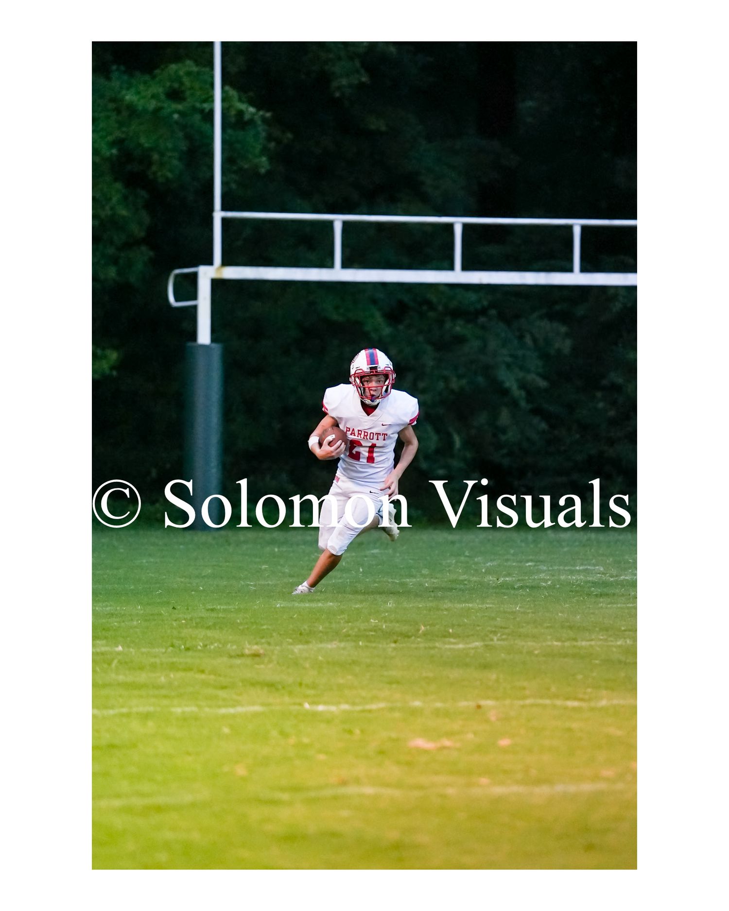 Football player in white uniform runs along sideline carrying ball during outdoor game.